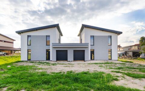 Front view of twin modern houses with a symmetrical architectural design under a cloudy sky.