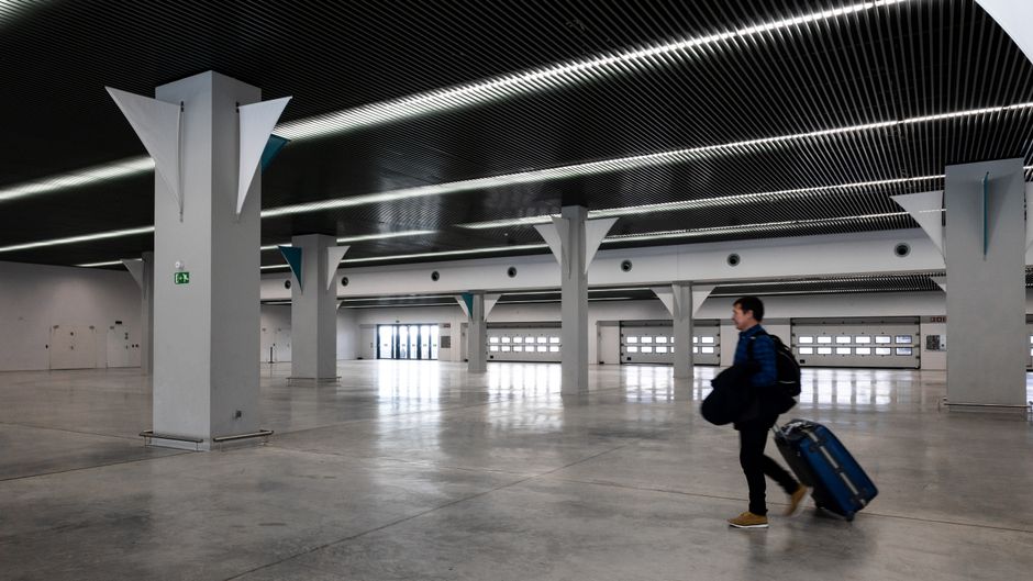 A man with luggage walking through a spacious, modern, empty airport hall.