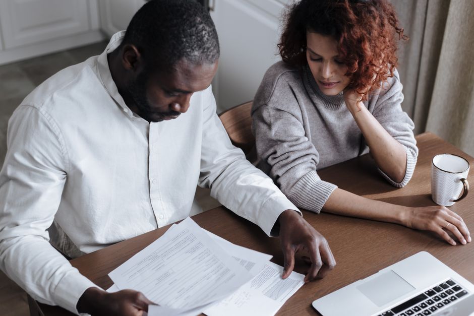 A couple reviews important documents together at a home desk with a laptop.