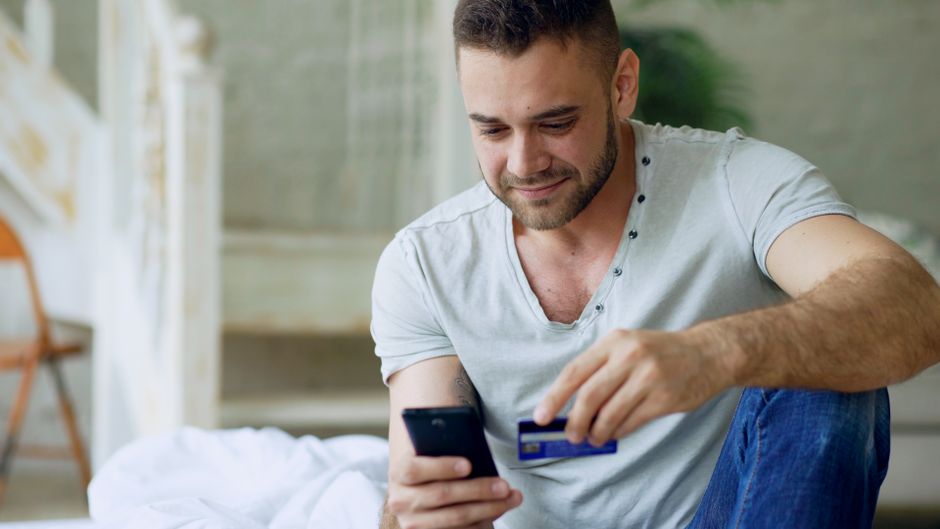 Smiling man using smartphone for online shopping in cozy indoor setting.