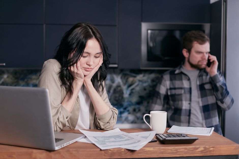 Couple dealing with financial stress at home, surrounded by bills and a laptop.