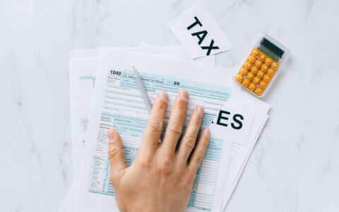 Close-up of a hand on tax form 1040 with a calculator on a desk.