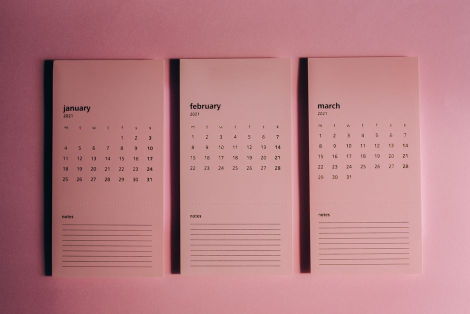 Overhead view of modern paper calendars with horizontal lines for notes and monthly dates on pink background