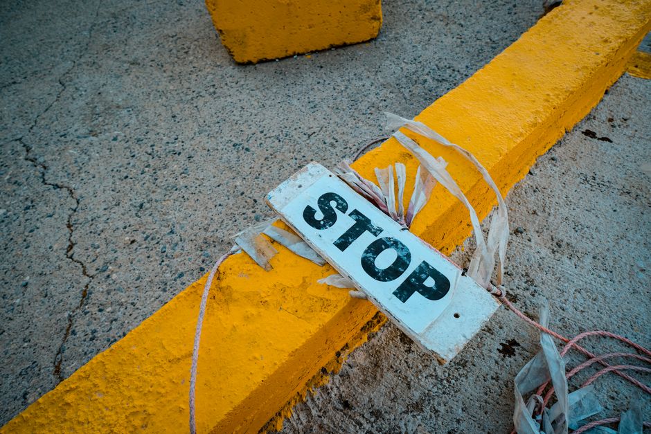 A worn 'STOP' sign placed on a cracked concrete pavement next to a yellow curb.