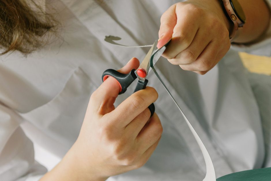 Teenager's hands using scissors to cut paper in an indoor setting.