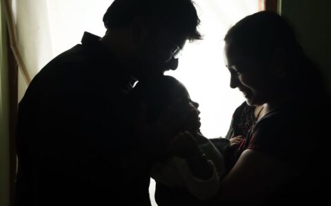 Silhouette of parents lovingly holding their baby indoors, exuding joy and warmth.