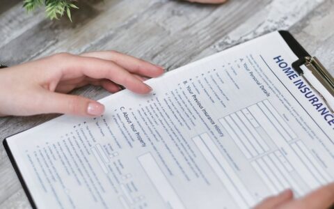 Close-up of hands holding a home insurance document indoors, showing personal details section.