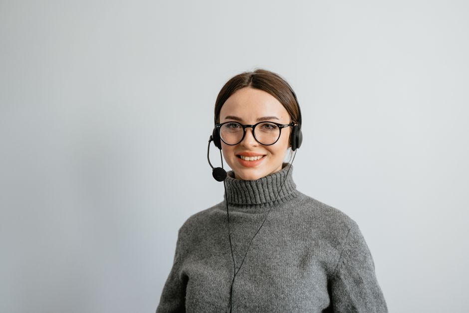 Smiling female call center agent wearing headphones and a gray sweater, ready to assist.