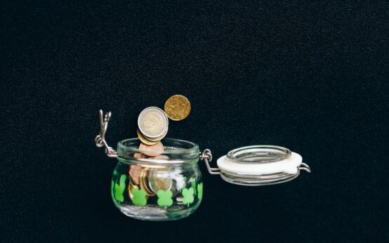 Glass jar with coins falling into it on a black background, symbolizing savings.