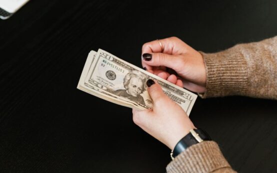 Close-up of hands counting a stack of US dollar banknotes on a dark table.