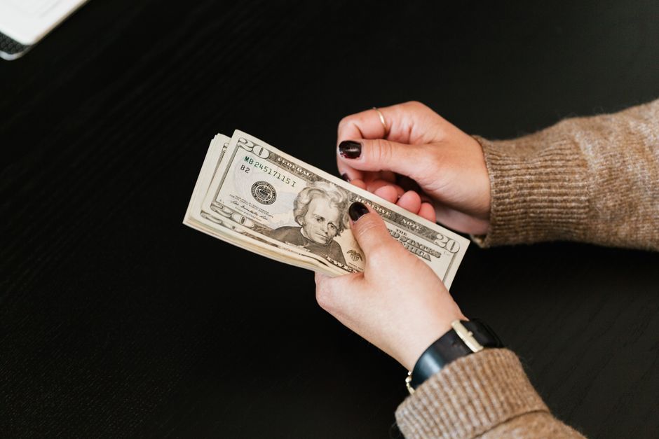 Close-up of hands counting a stack of US dollar banknotes on a dark table.