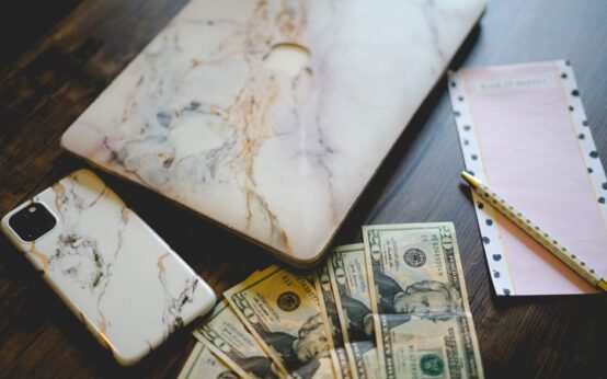 Stylish workspace with marble tech accessories, US currency, and a notepad on a wooden desk.