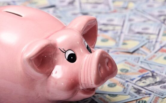 Close-up image of a shiny pink piggy bank surrounded by US hundred dollar bills, symbolizing savings and finance.