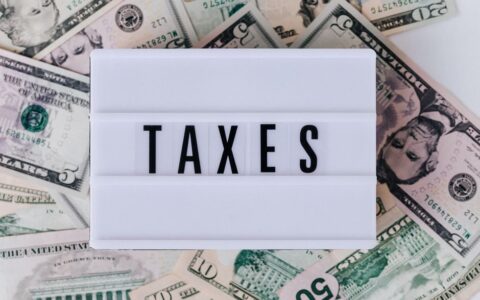 Top view of white vintage light box with TAXES inscription placed on stack of USA dollar bills on white surface