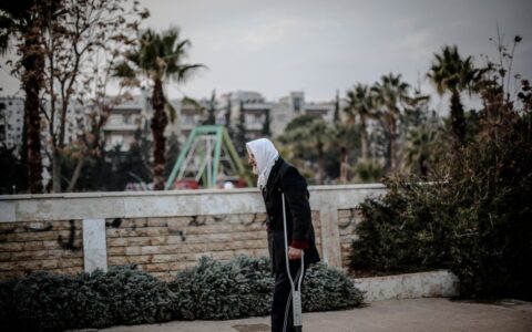 Elderly woman using a crutch walking outdoors in Idlib, Syria.