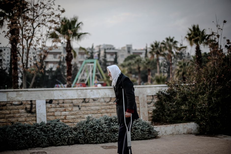 Elderly woman using a crutch walking outdoors in Idlib, Syria.