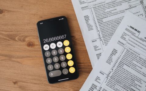 Overhead view of smartphone calculator and tax forms on a wooden table.