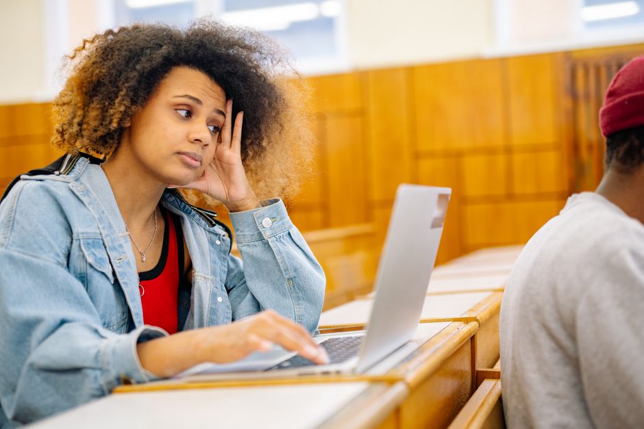 A young woman sits in a classroom, focused on her laptop, portraying a study session.
