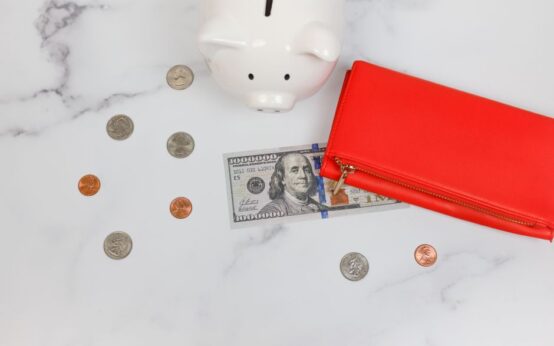 Overhead view of piggy bank, red wallet, and US dollars on marble surface.